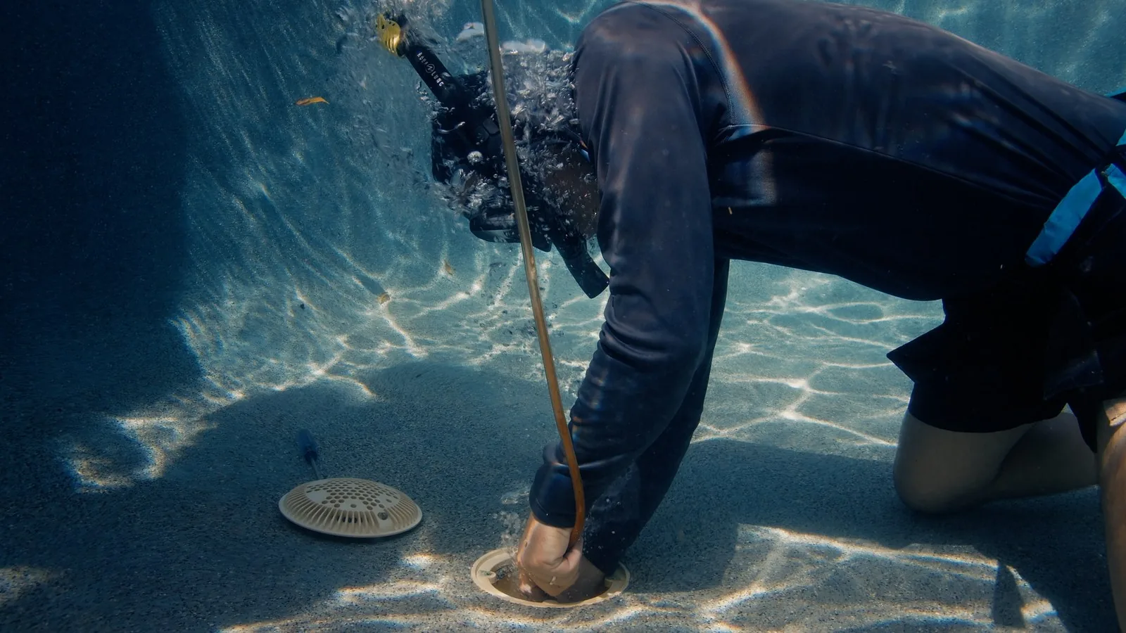 Diver from Advanced Leak Detection inspecting a pool main drain underwater without draining the pool